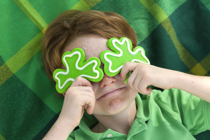 Redhead and freckle face Irish boy leprechaun with shamrock cookies over his eyes. Smiling Irish child wearing green on St. Patrick's day