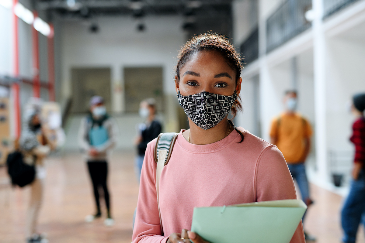 Student at school with mask on holding books